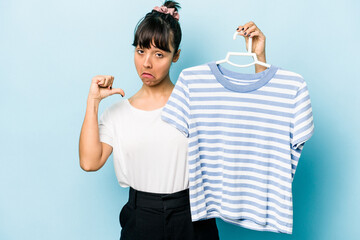 Young hispanic woman holding a t-shirt on a hanger isolated on blue background feels proud and self...