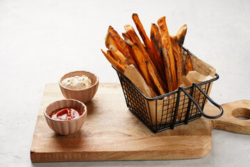 Healthy homemade oven baked sweet potato fries in a black deep frying basket net grid, wooden...