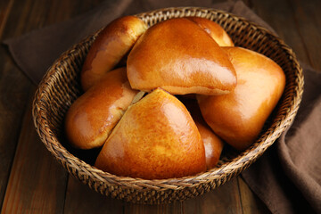 Wicker basket with delicious baked pirozhki on wooden table