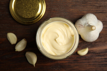 Jar of delicious mayonnaise and fresh garlic on wooden table, flat lay
