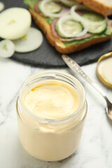 Obraz na płótnie Canvas Jar of delicious mayonnaise near fresh sandwich on white marble table
