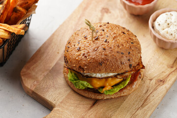 Vegetarian hamburger with cheddar cheese in whole grain bun and homemade oven baked sweet potato fries in a black deep frying basket net grid, wooden board, with ketchup sauce and mayonnaise
