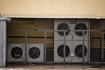 Maszynownia - agregaty chłodnicze . Przemysłowe klimatyzatory ( air conditioning  ) na zewnątrz budynku pod dachem z karbowanej blachy , za ogrodzeniem z siatki stalowej .