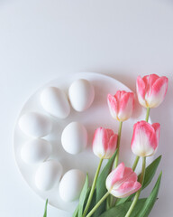white chicken eggs on a white plate on a white table with pink tulips