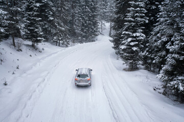 Aerial drone photography of a winter forest and back of a car on a snowy curvy road