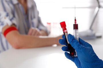 Nurse holding syringe and sample tube with blood in clinic, closeup. Space for text