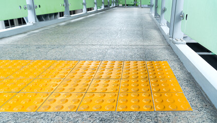 Yellow braille block with buttons raised above the surface. For warning to be cautious when pedestrians touch the embossed surface. Before going down the stair of overpass.