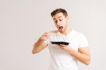 Portrait of handsome young man with enjoying eating fresh tasty sushi rolls with chopsticks on...
