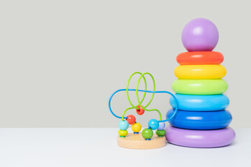 A set of children's educational toys on a gray background. A colored plastic pyramid of rings and a maze with wooden beads. Games for the development of logic