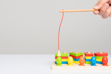 A hand with a toy fishing rod with a magnet shows how to use a wooden sorter toy with colored...