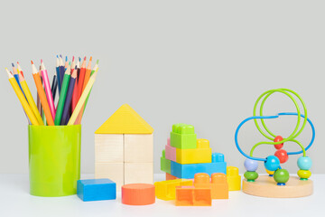 A set of children's educational toys on a gray background. Colorful pencils for drawing, a wooden and plastic constructor and a maze with beads for the development of logic.