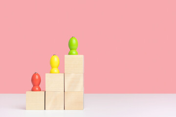 The concept of growth and development in business. Three wooden pawns stand on wooden cubes built in the form of a pyramid ladder. Copyspace on pink background