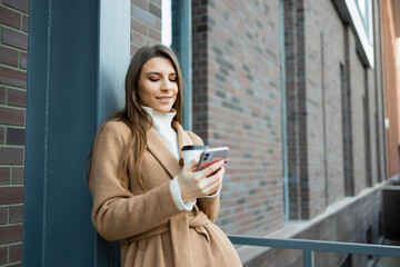 Young woman outdoors with a cup of coffee using smartphone.