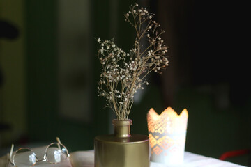 Open book, reading glasses, candle holder with lit candle and vase with gypsophila flowers. Dark background, selective focus.