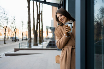 Pretty woman in brown coat with coffee cup outdoors