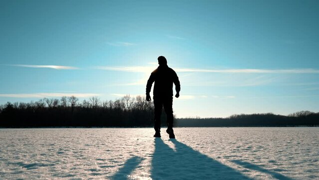 Silhouette of a man walking into the distance through the snow during sunset. A loner walks across a large meadow of snow. Failure and loneliness.