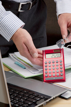 Budget Manager mit Taschenrechner am Schreibtisch bei der Kostenanalyse und Kalkulation 