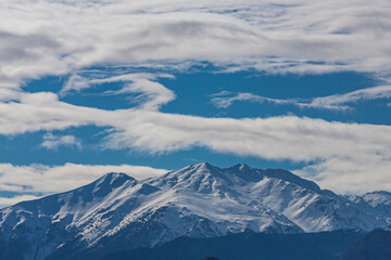 Panoramic view of high mountains with snow-capped peaks against a blue sky with clouds