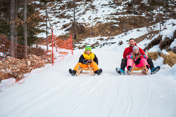 Family sledding on the snow and having fun in winter. - obrazy, fototapety, plakaty