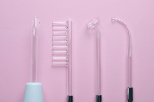 Modern darsonval with different nozzles on pink background, flat lay. Microcurrent therapy