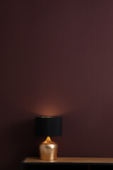 Wooden table with lamp near brown wall in room, space for text