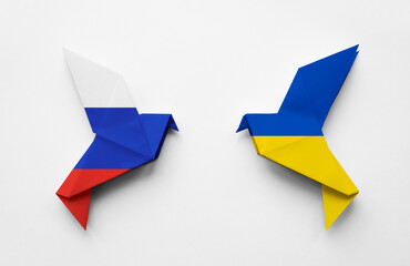 Two origami paper doves in the colors of the flags of Russia and Ukraine on a white background. The...