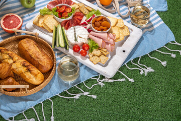 Picnic blanket with charcuterie boards, healthy food and wine in park on the grass on sunny day.