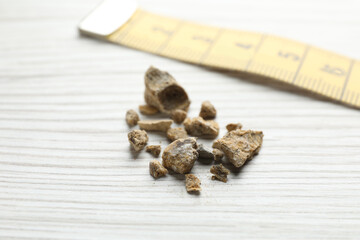 Kidney stones and measuring tape on white wooden table, closeup
