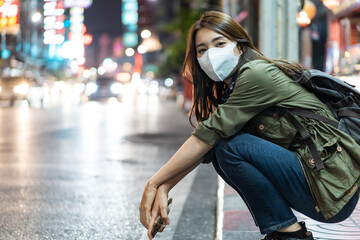 Asian young woman backpacker wear mask, wait for bus in city at night. 