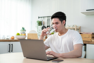 Asian business man drinking miniral water while sit working from home.