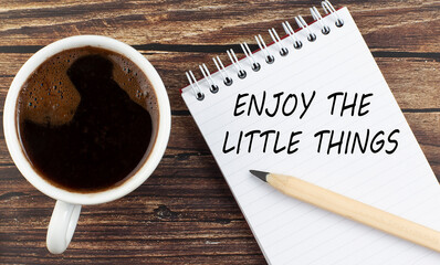 ENJOY THE LITTLE THINGS text on notebook with coffee on the wooden background