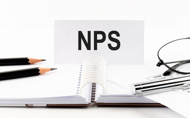 Text NPS on paper card,pen, pencils,glasses,financial documentation on table - business concept