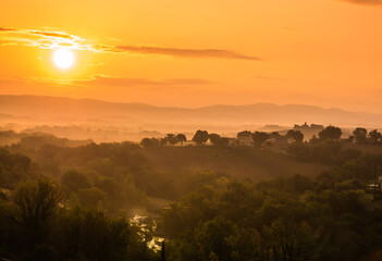 paesaggio con colori caldi e riflessi argentei di un fiume su una ampia vallata all'alba in Toscana, Italia