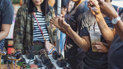 Tourists choosing and shopping fashionable variety sunglasses for sale with nice discounted lenses while touring at a local street market. Improves vision and reduces UV glare. Selective focus.