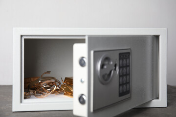 Open steel safe with gold bars and jewelry on grey table against light background