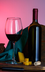 glass and bottle of red wine with hard cheese on a pink background, rustic style.
