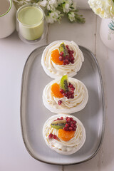 dessert pavlova with cream and fruits on gray plate white scandic ground white spring flowers matcha tea