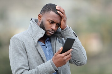 Worried man with black skin checking phone in winter