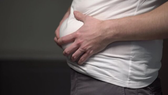Fat man. Man touches his stomach. Belly, overweight. Oversize person holds skin.