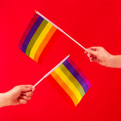 Close Up Studio Shot Of Two Female Hands Holding LGBT Rainbow Flags Against Red Background