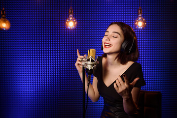 Young woman singer with headphones  is recording a song in an audio recording studio.