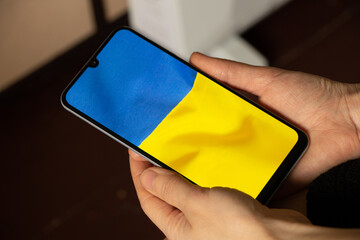 The national flag of Ukraine as a background on the phone in the hands of a woman, peace in Ukraine, no war, free