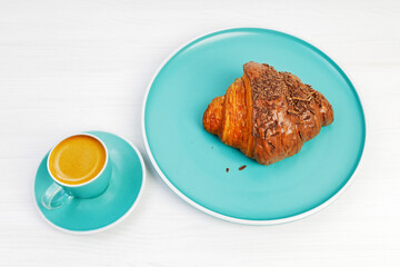 Croissant with chocolate and cup of coffee espresso on white wooden table.