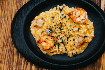 Risotto with shrimps and a flower on a black plate.