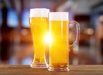 Glass mugs of cold beer with foam served on wooden table at night