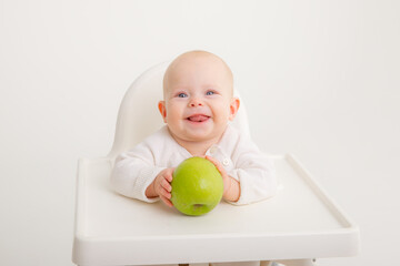 Fototapeta premium baby girl in baby chair eating apples on white background. Baby first solid food