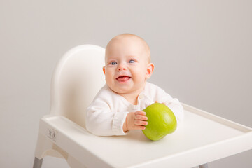 baby girl in baby chair eating apples on white background. Baby first solid food