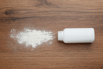 Bottle and scattered dusting powder on wooden background, top view. Baby cosmetic product