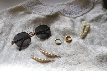 Vintage white floral blouse, round sunglasses, gold rings and pearl hair barrettes. Selective focus.