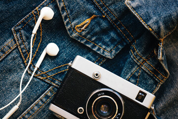 Film camera and white wired headphones lie against background of denim. Fashionable hipster...